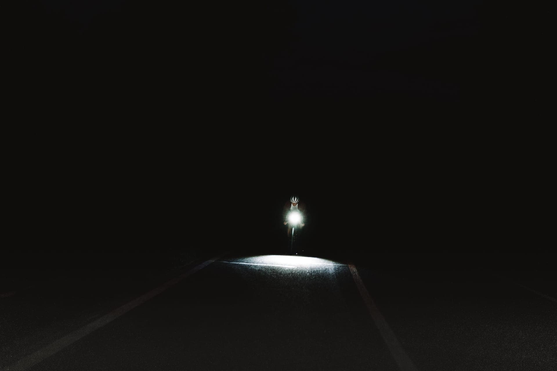 A bicycle headlight beam casting a defined pool of light on a dark road.