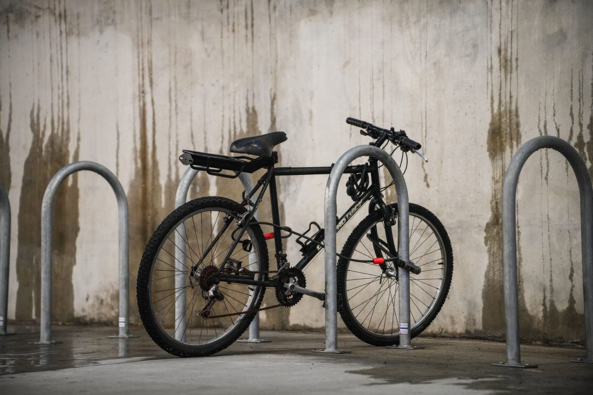 A bicycle secured to a city bike rack beside a concrete wall.