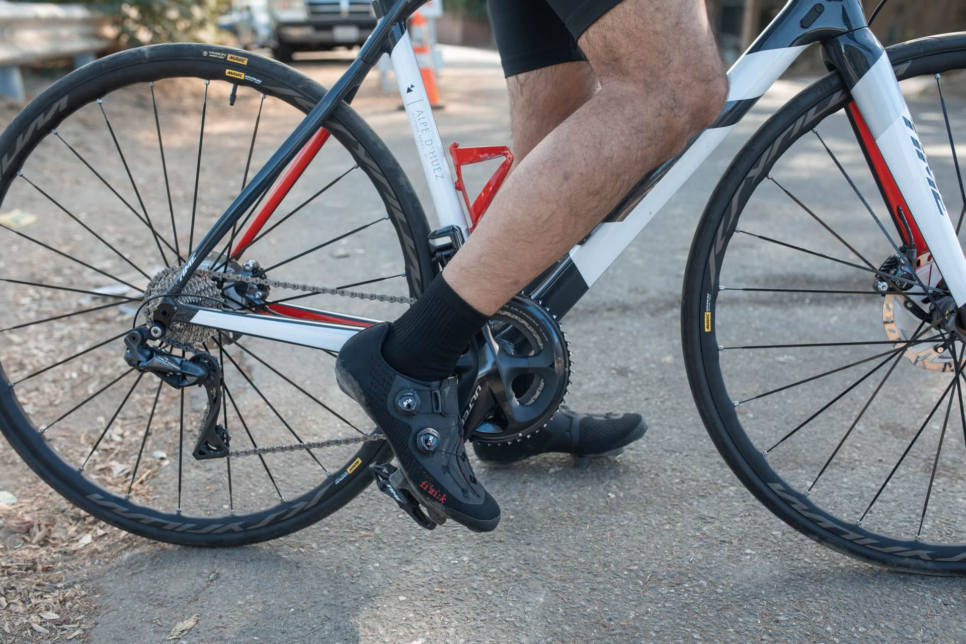 A road cycling shoe clipped into a pedal, with the drivetrain in view.
