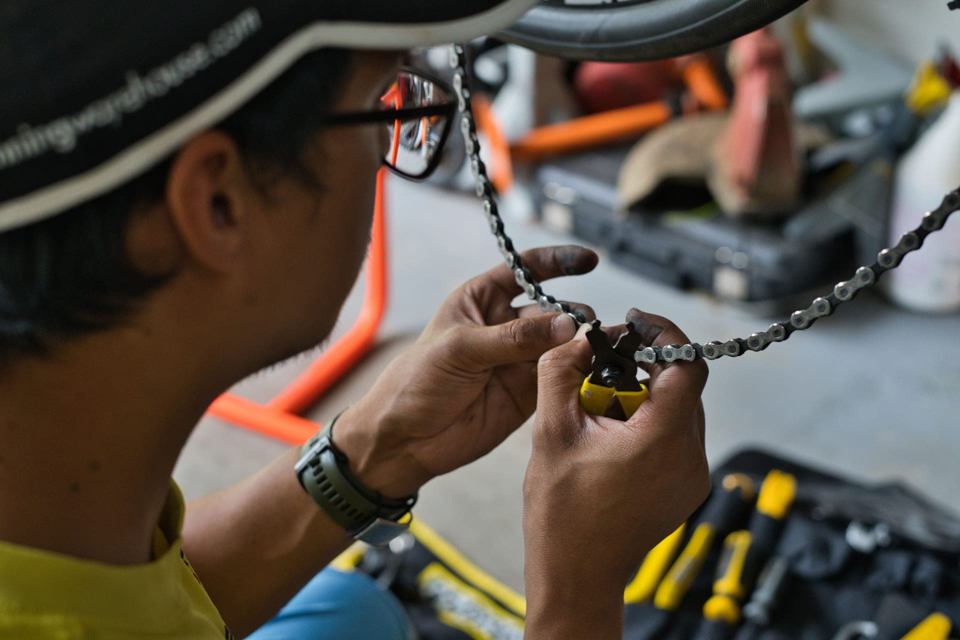 Hands cleaning a bicycle chain with a brush over a workbench.