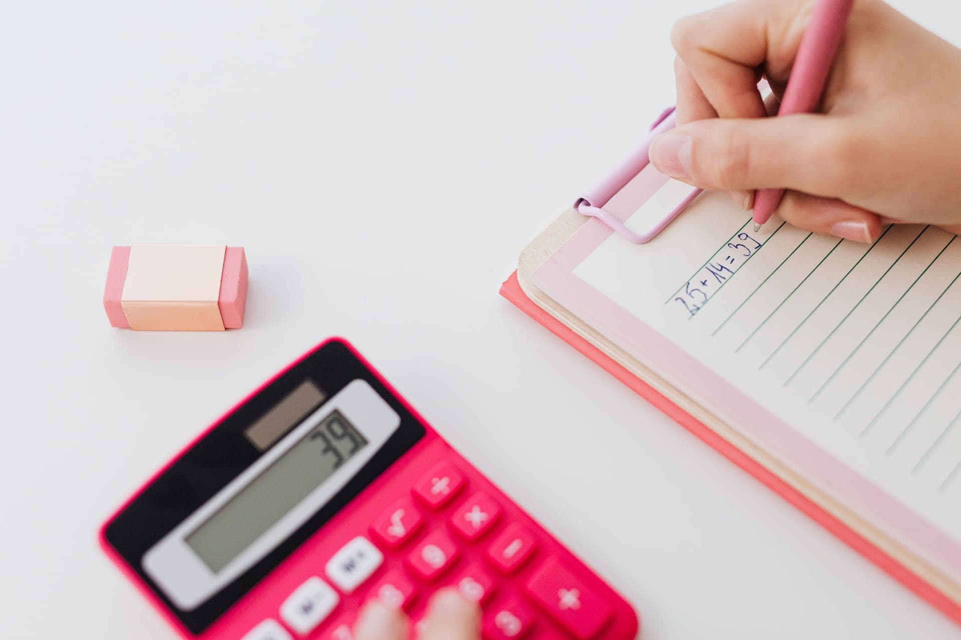 A notebook, calculator and pen on a desk under a work lamp.